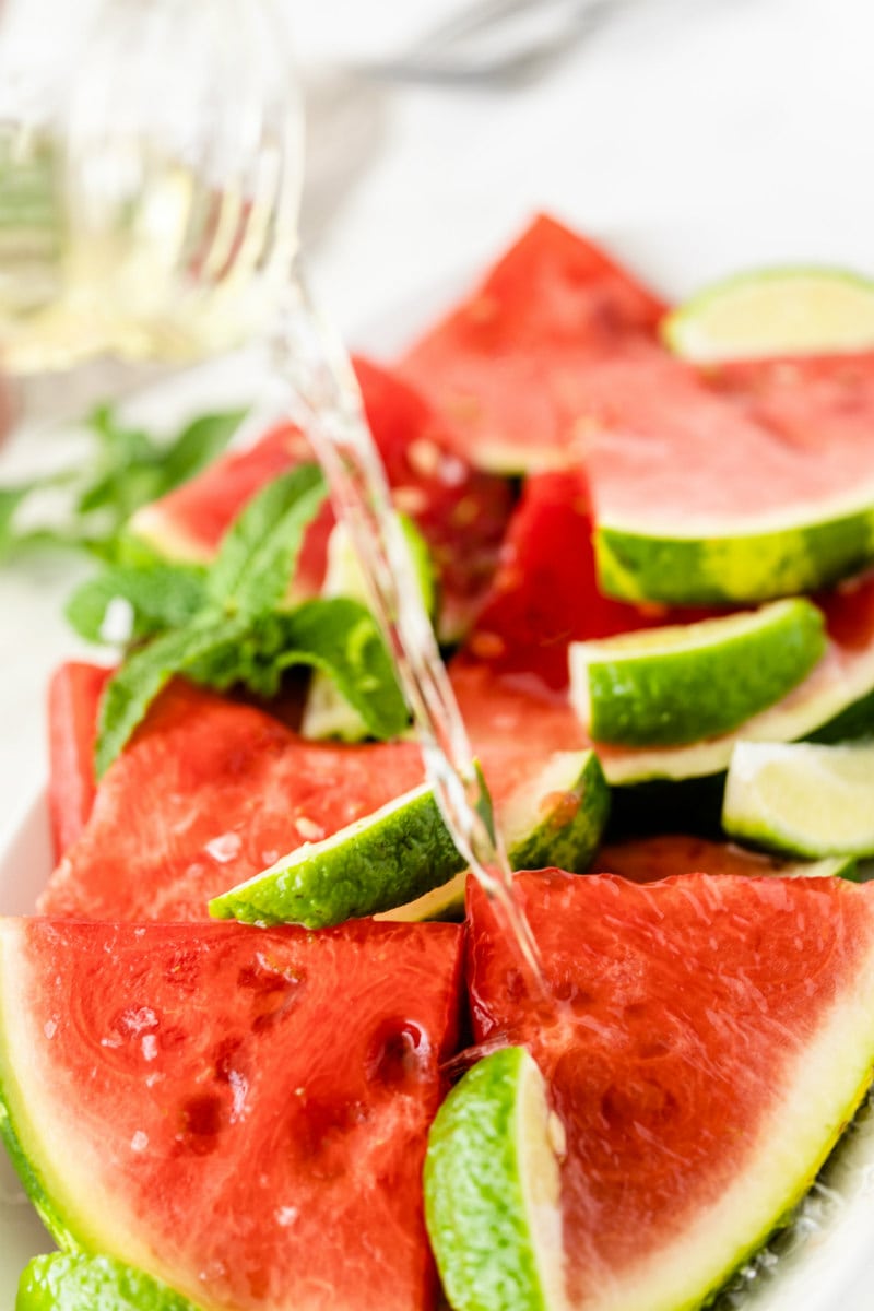 pouring tequila onto watermelon with lime wedges
